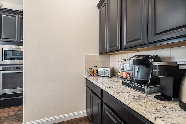 kitchen featuring dark wood finished floors, stainless steel appliances, decorative backsplash, light stone countertops, and baseboards