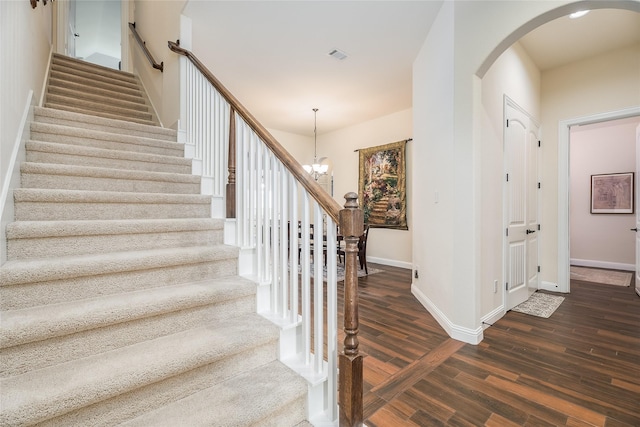 stairs with a chandelier, arched walkways, wood finished floors, and baseboards