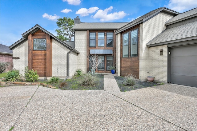 view of front of house with concrete driveway, brick siding, a chimney, and an attached garage