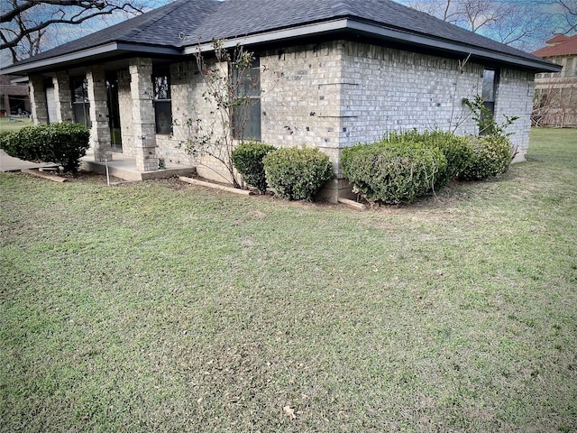 view of side of home featuring a yard, brick siding, and roof with shingles