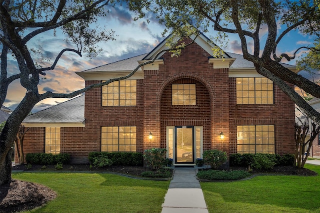 traditional home featuring roof with shingles, a front yard, and brick siding