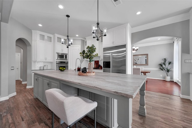 kitchen with arched walkways, white cabinetry, visible vents, and built in appliances