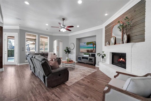 living room with arched walkways, baseboards, ornamental molding, a brick fireplace, and dark wood finished floors