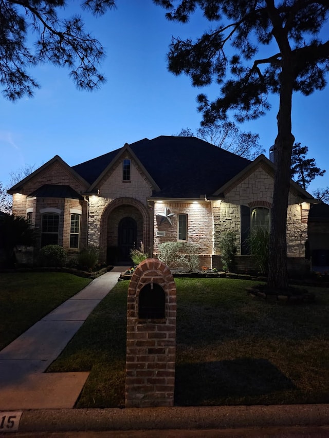 french provincial home with a front yard and stone siding