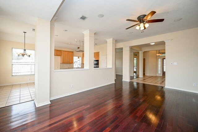 unfurnished living room featuring ceiling fan with notable chandelier, hardwood / wood-style floors, visible vents, and ornate columns