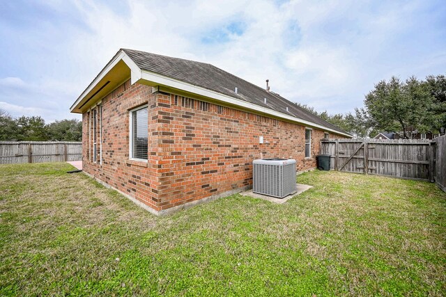 rear view of house featuring central air condition unit, a yard, a fenced backyard, and brick siding