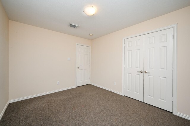 unfurnished bedroom with dark colored carpet, a closet, visible vents, and baseboards