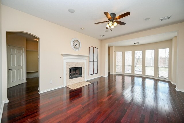 unfurnished living room with arched walkways, a tile fireplace, dark wood-style flooring, visible vents, and baseboards