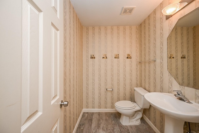 bathroom with wallpapered walls, baseboards, visible vents, toilet, and wood finished floors