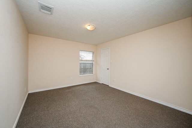 empty room featuring a textured ceiling, dark carpet, visible vents, and baseboards