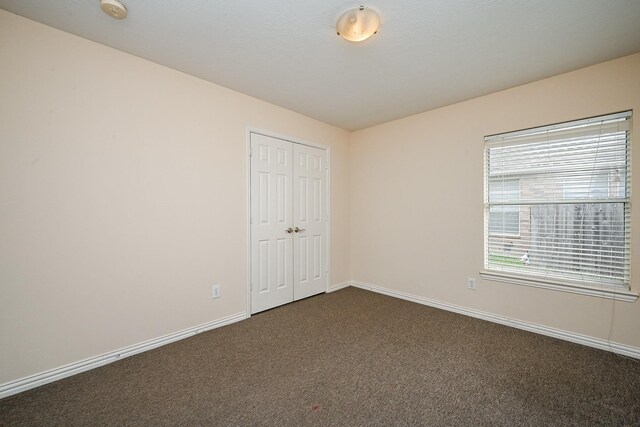 unfurnished bedroom with dark colored carpet, a closet, and baseboards