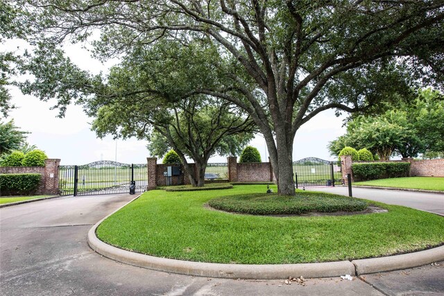 view of community with driveway, a gate, fence, and a lawn