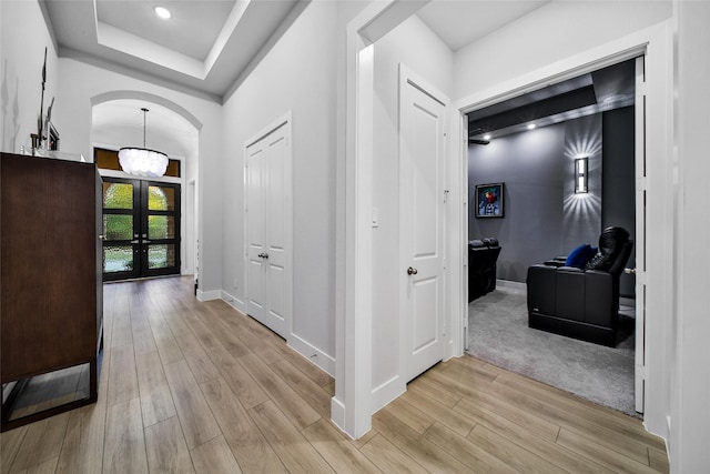 hall featuring arched walkways, baseboards, light wood-style flooring, french doors, and a notable chandelier