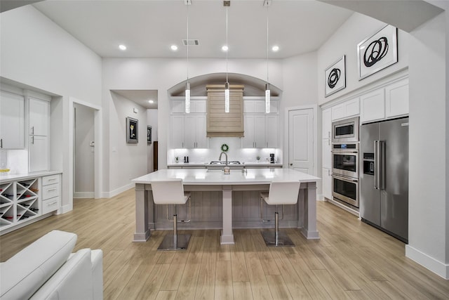 kitchen featuring stainless steel appliances, light countertops, visible vents, a high ceiling, and white cabinets