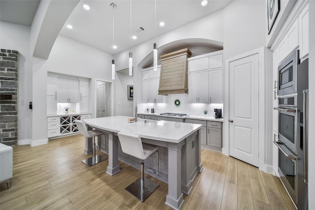 kitchen with visible vents, a towering ceiling, custom range hood, appliances with stainless steel finishes, and light wood-style floors