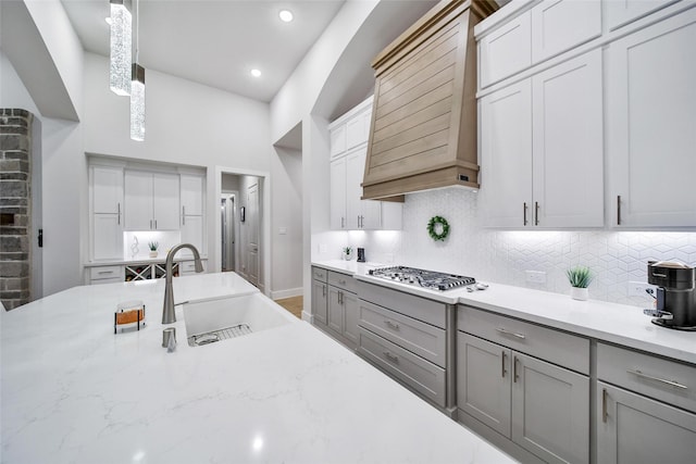 kitchen featuring gray cabinets, a sink, stainless steel gas cooktop, and custom exhaust hood