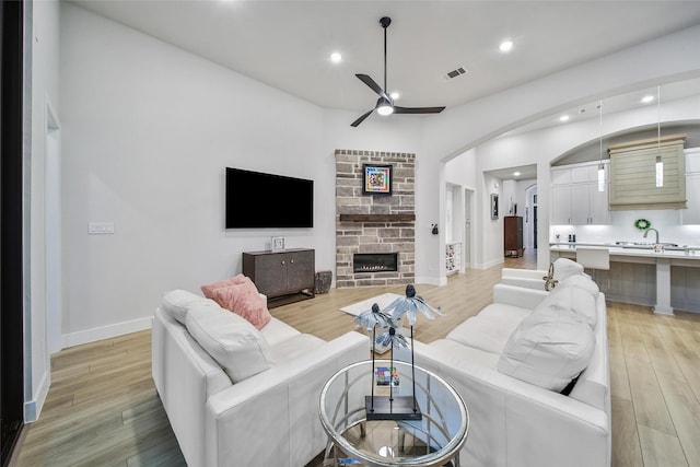 living room with ceiling fan, a stone fireplace, light wood-style flooring, recessed lighting, and visible vents