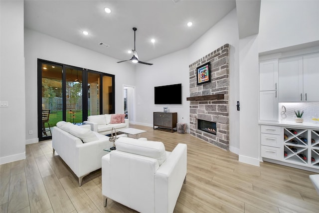 living area with light wood-style flooring, baseboards, a ceiling fan, and a stone fireplace