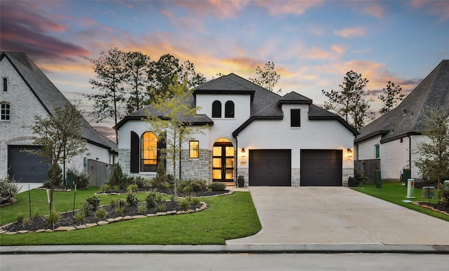 french provincial home with a garage, stone siding, driveway, and a front lawn