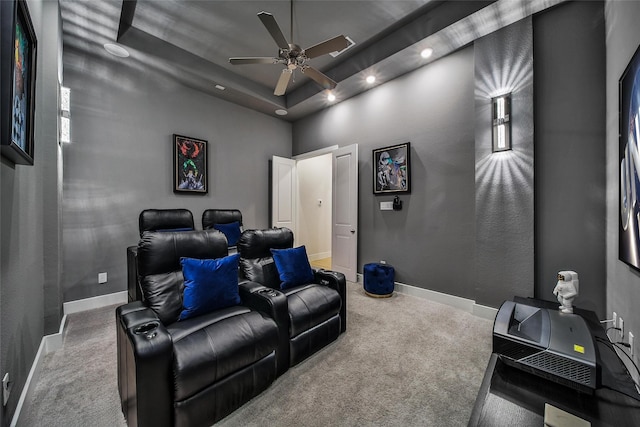 carpeted cinema with a tray ceiling, a ceiling fan, and baseboards