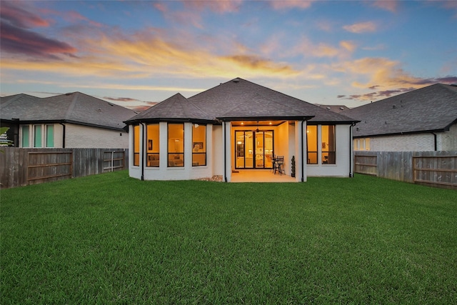 back of house with a fenced backyard, a shingled roof, and a yard