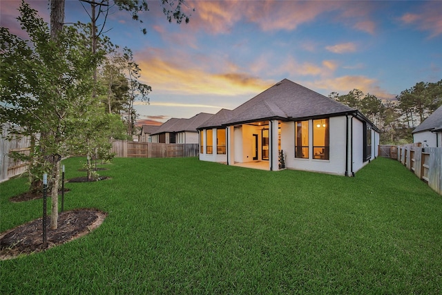 back of property with a shingled roof, a fenced backyard, a yard, and a patio