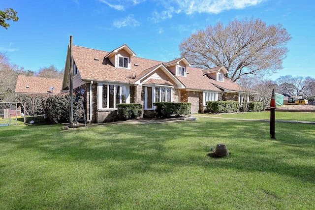 cape cod home featuring brick siding, a front lawn, and roof with shingles