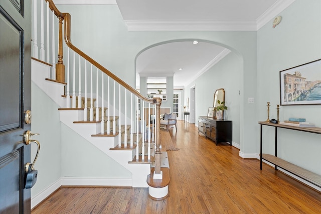 entryway with arched walkways, ornamental molding, wood finished floors, and stairs