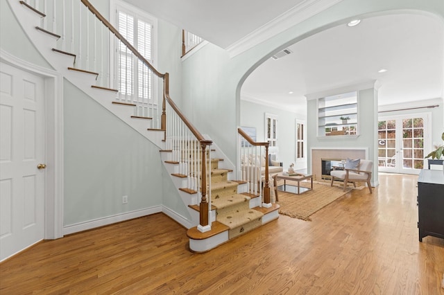 stairs with arched walkways, crown molding, visible vents, wood finished floors, and baseboards