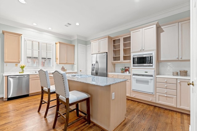 kitchen with appliances with stainless steel finishes, a kitchen bar, a kitchen island, and light wood-style floors