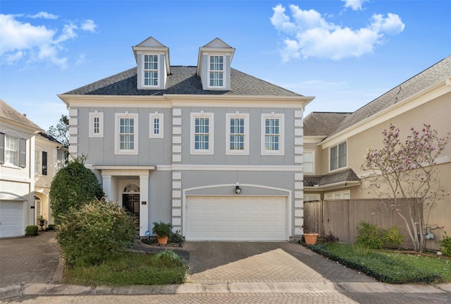 colonial house with a garage, a shingled roof, decorative driveway, and stucco siding