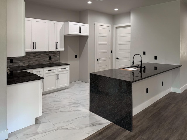 kitchen featuring a peninsula, marble finish floor, a sink, white cabinetry, and backsplash