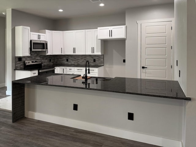 kitchen featuring dark stone countertops, appliances with stainless steel finishes, white cabinets, and a sink