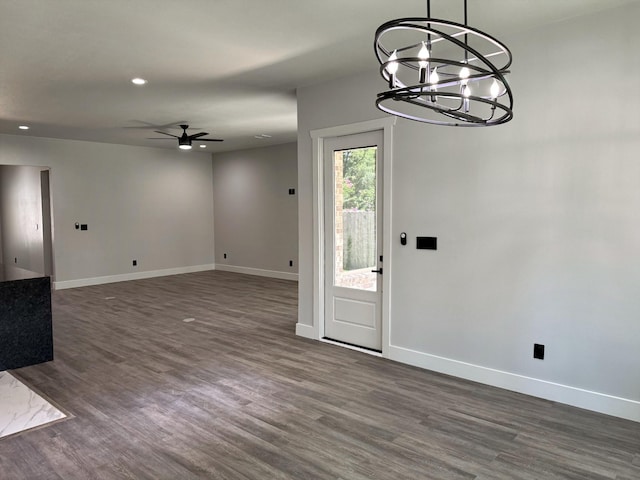 unfurnished dining area with recessed lighting, baseboards, dark wood-type flooring, and ceiling fan with notable chandelier