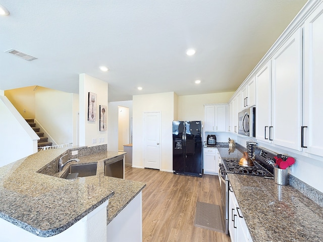 kitchen featuring light wood-style flooring, stainless steel appliances, a sink, visible vents, and dark stone counters