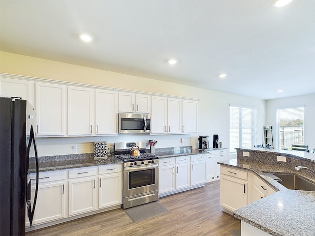 kitchen featuring appliances with stainless steel finishes, white cabinetry, a sink, dark stone countertops, and light wood-type flooring