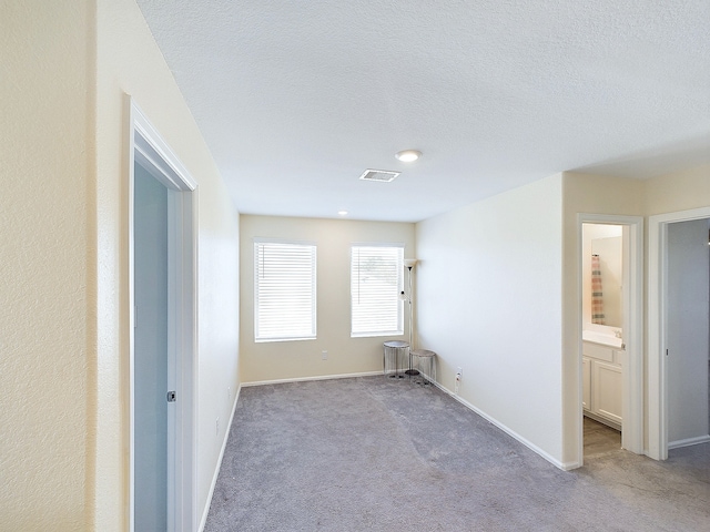 unfurnished room featuring a textured ceiling, carpet, visible vents, and baseboards