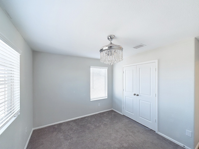 unfurnished bedroom featuring a chandelier, carpet floors, visible vents, baseboards, and a closet