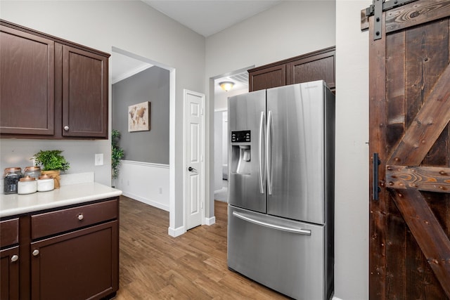 kitchen with stainless steel refrigerator with ice dispenser, light countertops, light wood-style flooring, a barn door, and dark brown cabinetry