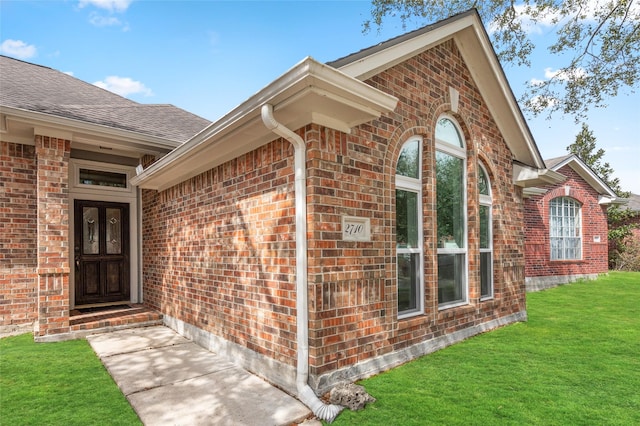 doorway to property featuring a yard and brick siding