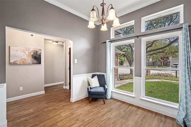 living area with baseboards, a chandelier, crown molding, and wood finished floors