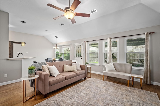 living area featuring lofted ceiling, visible vents, a barn door, a ceiling fan, and wood finished floors