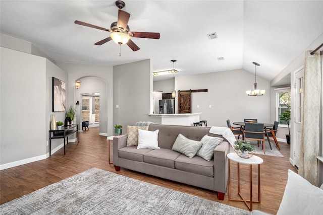 living room featuring arched walkways, lofted ceiling, a barn door, wood finished floors, and ceiling fan with notable chandelier