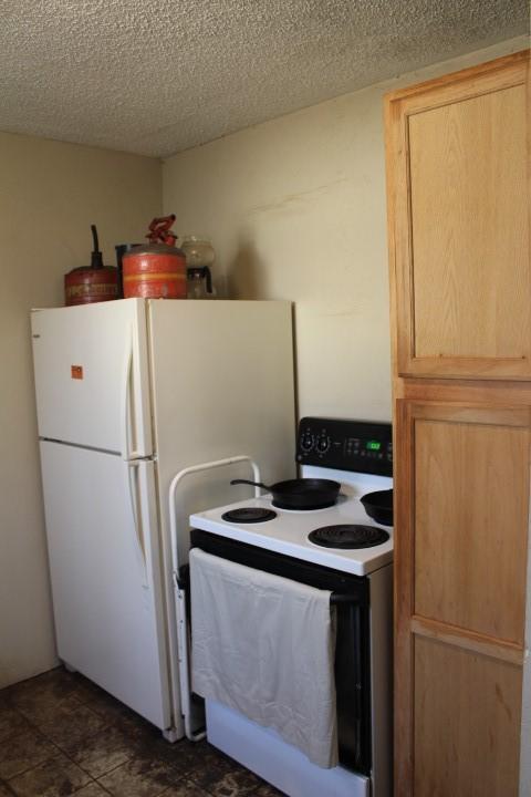 kitchen with white appliances, light brown cabinets, and a textured ceiling