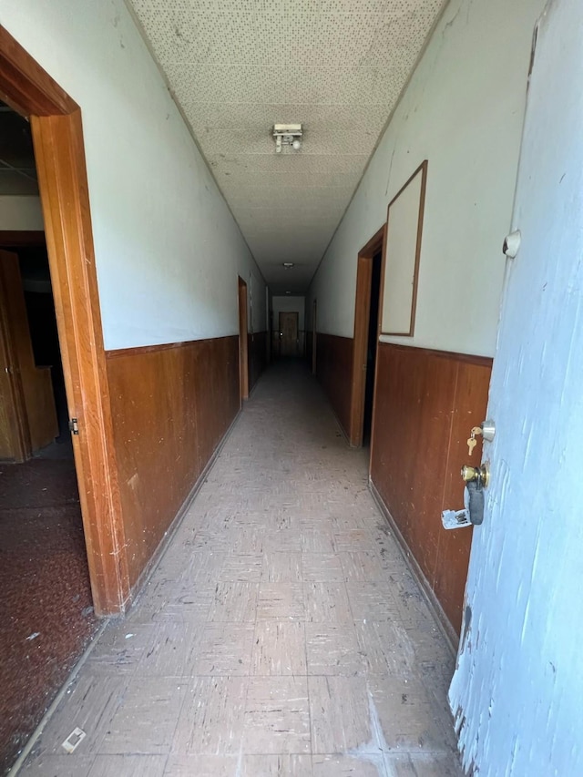 hallway featuring a wainscoted wall, wooden walls, and light floors