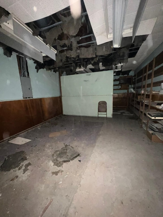 unfinished basement featuring a wainscoted wall, electric panel, and wooden walls