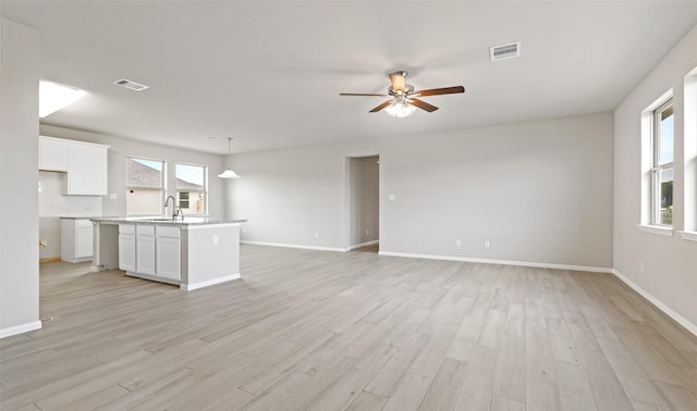unfurnished living room with visible vents, baseboards, a ceiling fan, and light wood finished floors