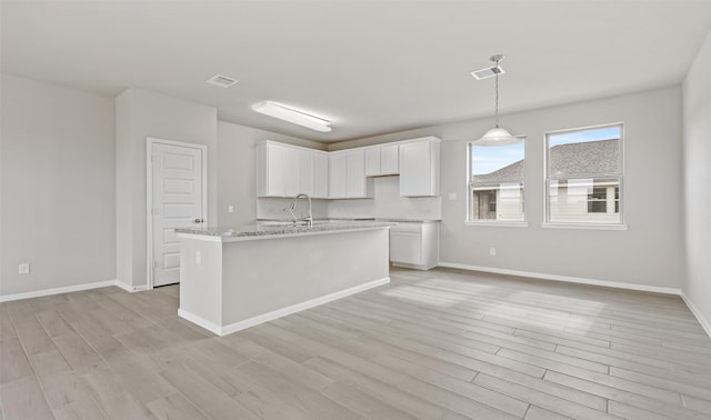 kitchen with visible vents, white cabinets, baseboards, an island with sink, and light wood-style floors
