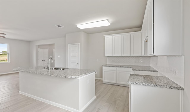kitchen with light stone countertops, light wood-style flooring, a sink, and backsplash