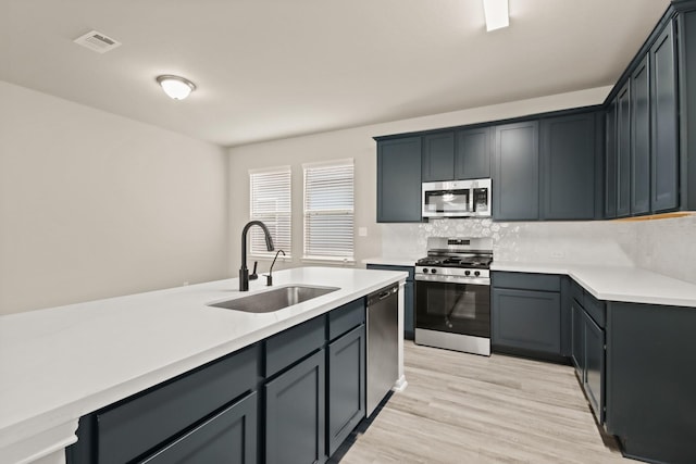 18798 Lucas Michael Way, New Caney, TX 77357 - kitchen featuring appliances with stainless steel finishes, a sink, decorative backsplash, light wood-type flooring, and light countertops